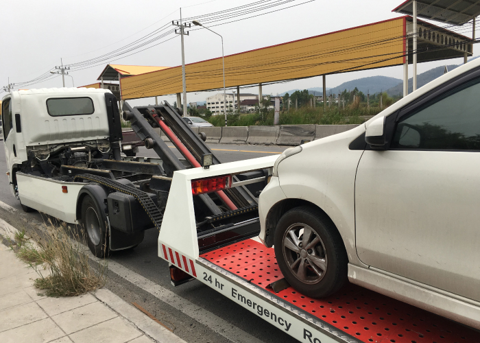 Una grúa de asistencia en carretera remolca un automóvil blanco sobre una plataforma roja con ranuras.